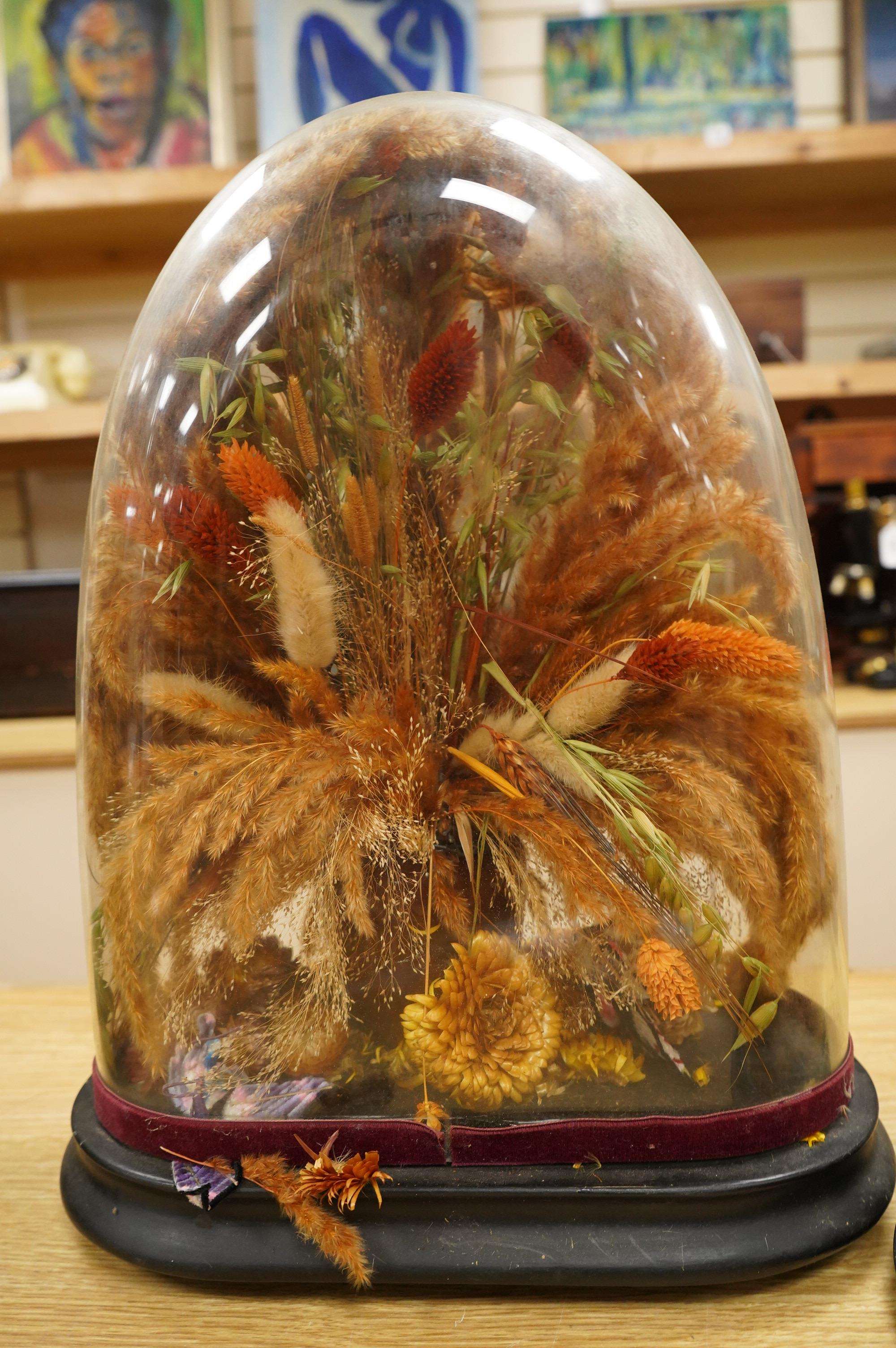 Two Victorian fauna displays under domes with ebonised bases, containing dried grasses and flowerheads, together with fabric butterflies, tallest 46cm, both af